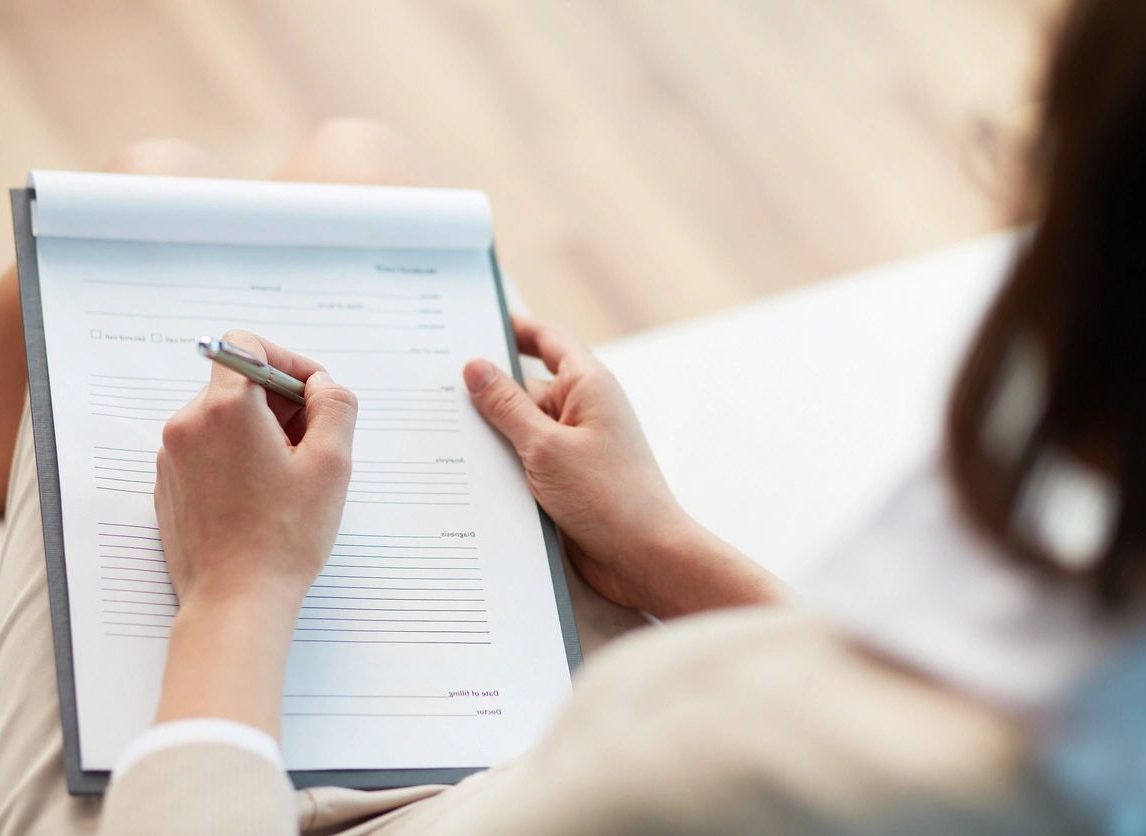 A person writing on paper with pen and pencil.